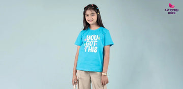 Smiling girl wearing blue graphic t-shirt and beige pants, kids fashion photoshoot