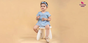 Smiling young girl in blue short-sleeve dress and headband sitting on white stool against beige background
