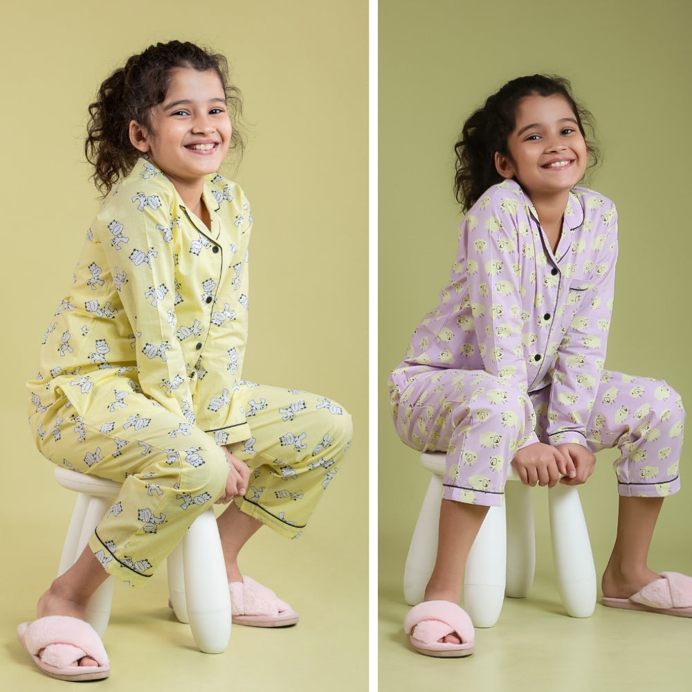 Girl wearing yellow and lavender printed night suits for kids, sitting on stool, smiling.