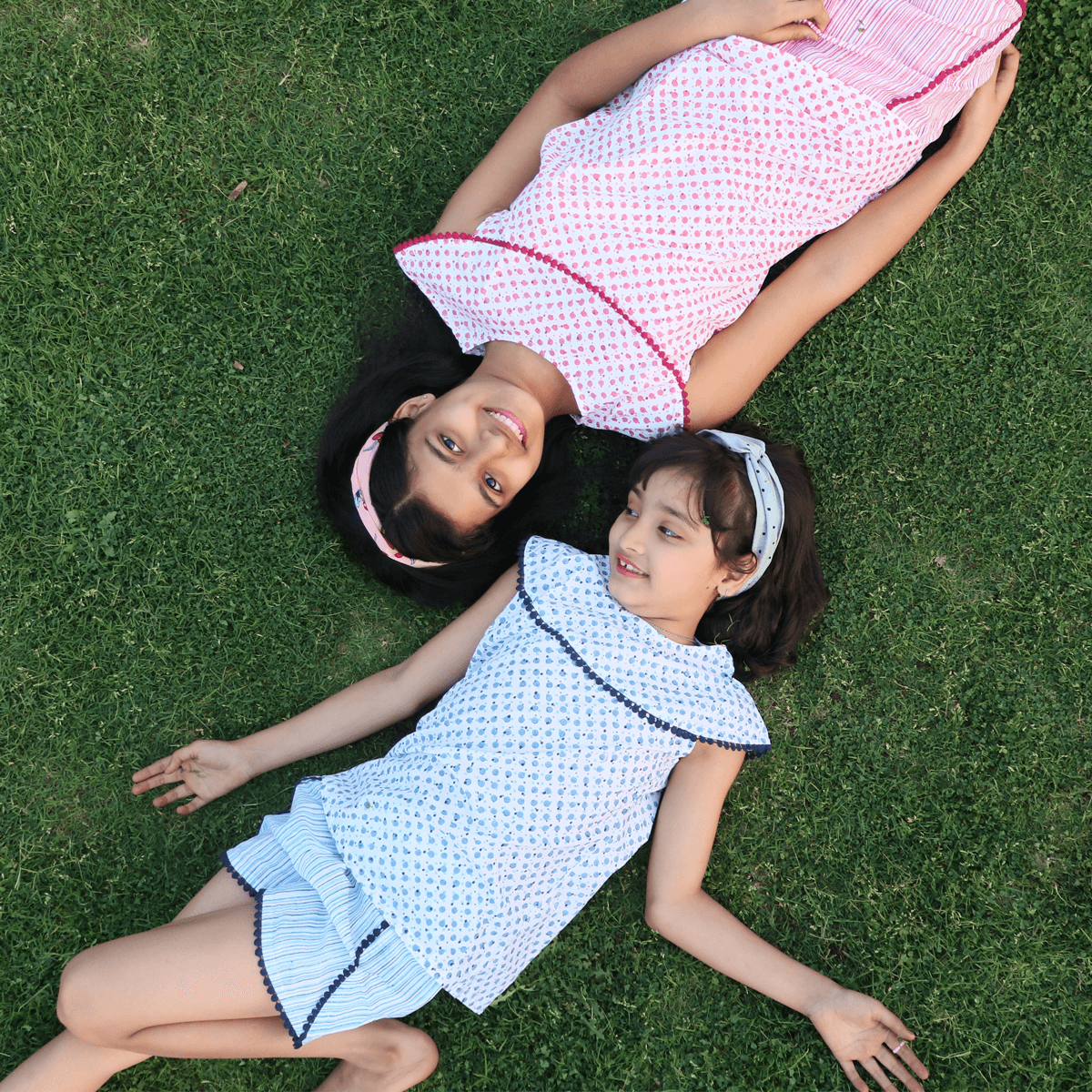 Two girls wearing matching printed summer outfits lying on grass, kids fashion clothing