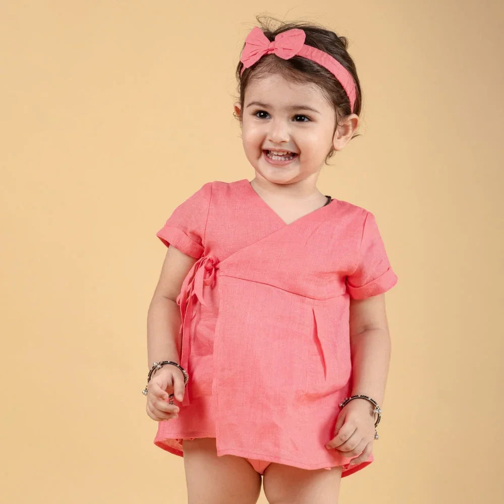 Smiling baby girl in pink dress with bow headband, stylish kids wear on beige background