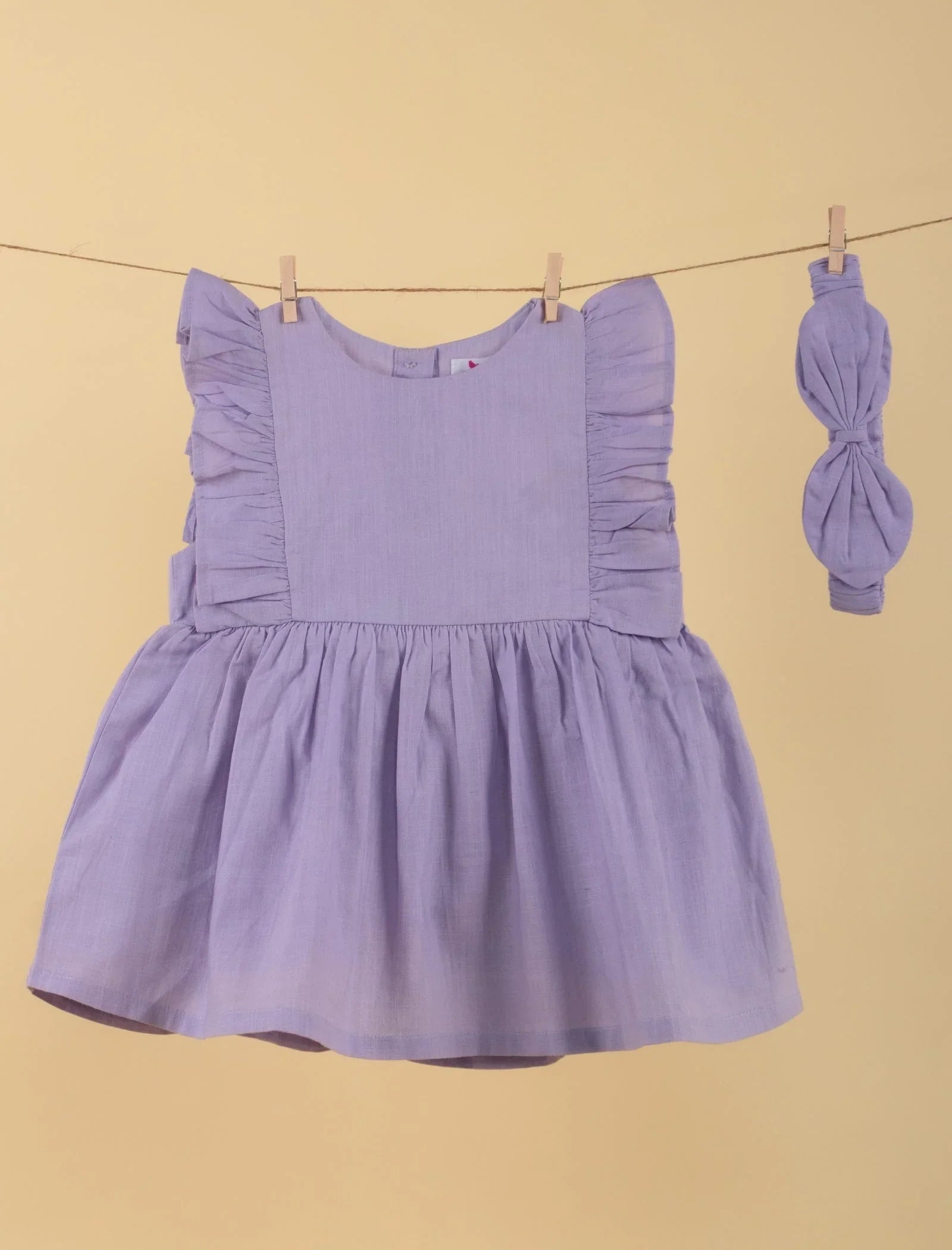 Lilac baby girl dress with ruffle sleeves and matching headband on a clothesline