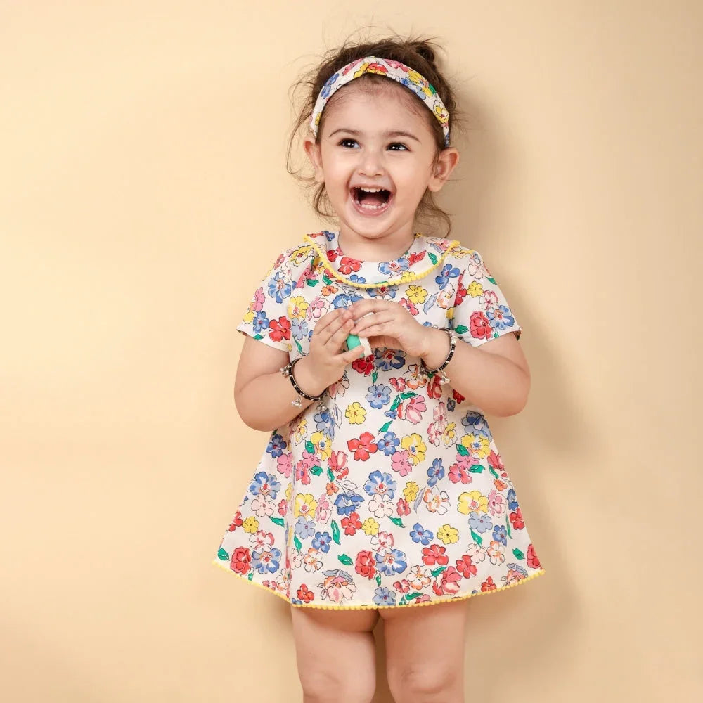 Smiling baby girl in a colorful floral dress and matching headband against beige background