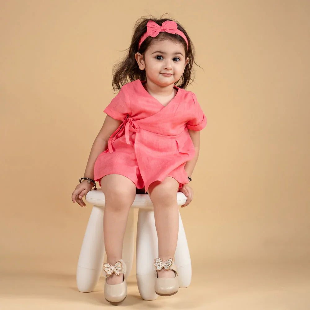 Toddler girl in a pink dress with matching headband and bow shoes, sitting on a white stool