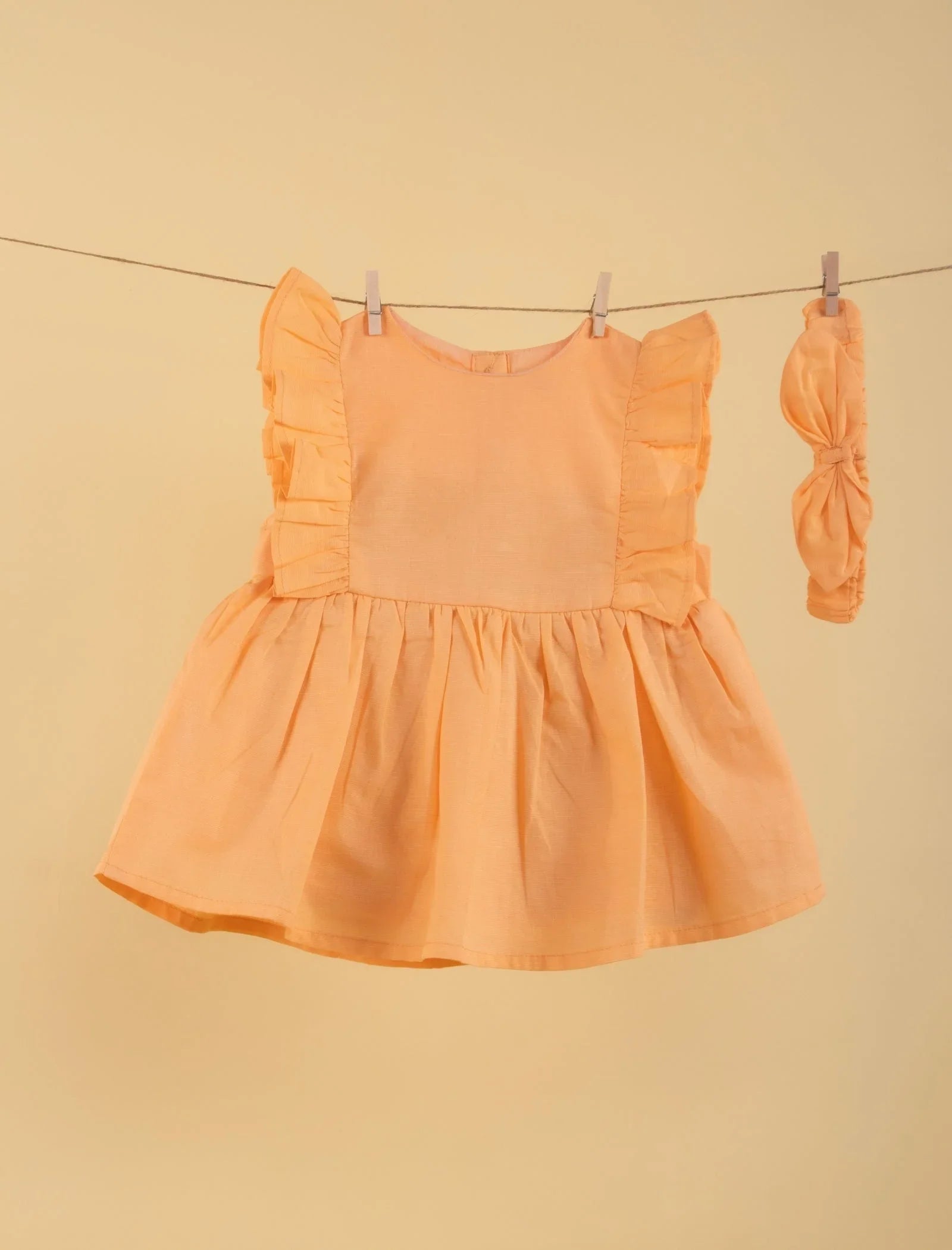 Peach ruffle baby girl dress with matching headband on beige background