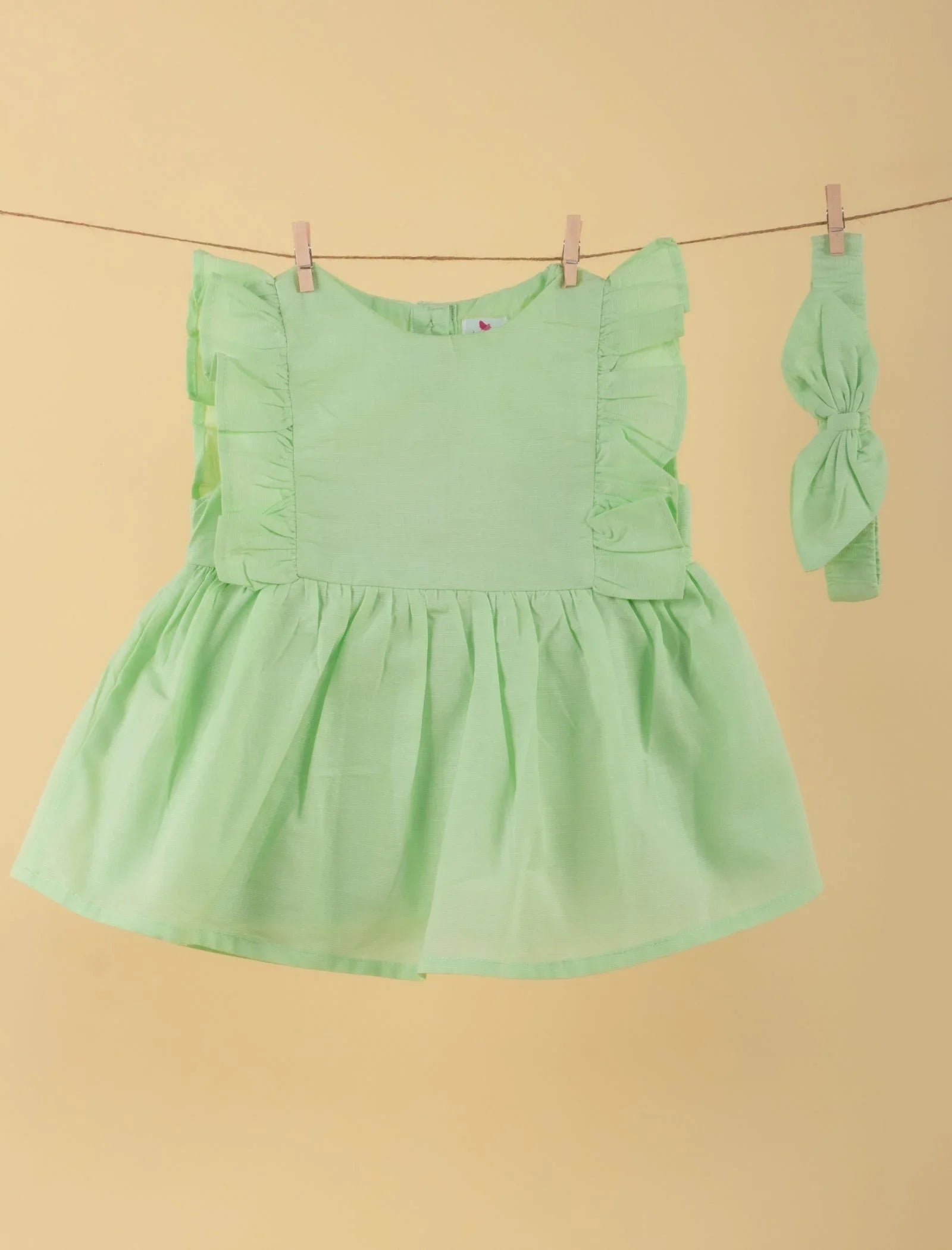 Light green baby girl dress with ruffle sleeves and matching headband on yellow background