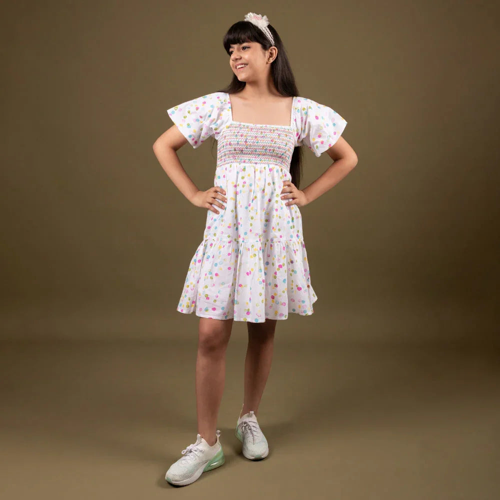 Girl in a short-sleeve white summer dress with colorful polka dots and sneakers