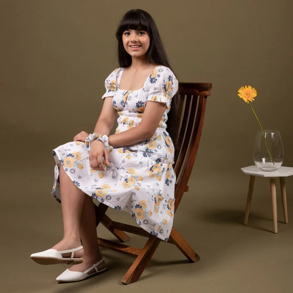 Girl in white floral dress sitting on chair, stylish kids fashion for ages 10-15 years