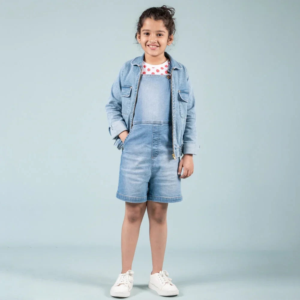 Girl wearing denim dungaree shorts, jean jacket, polka dot shirt and white sneakers