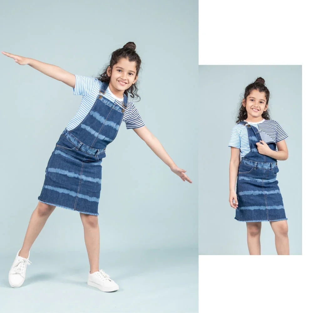 Girl wearing blue denim dungaree dress with striped t-shirt, kids fashion outfit