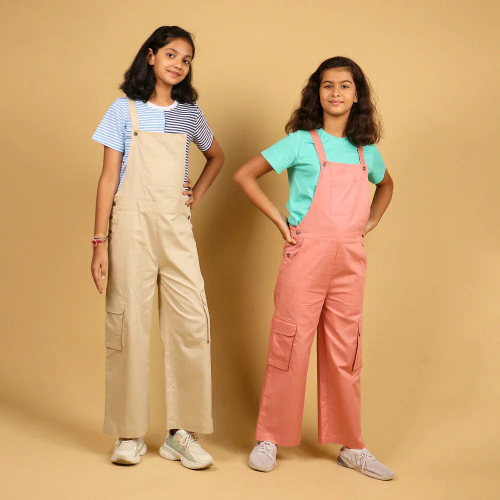 Two girls wearing stylish dungarees, one in beige and one in pink, posing against a beige background.