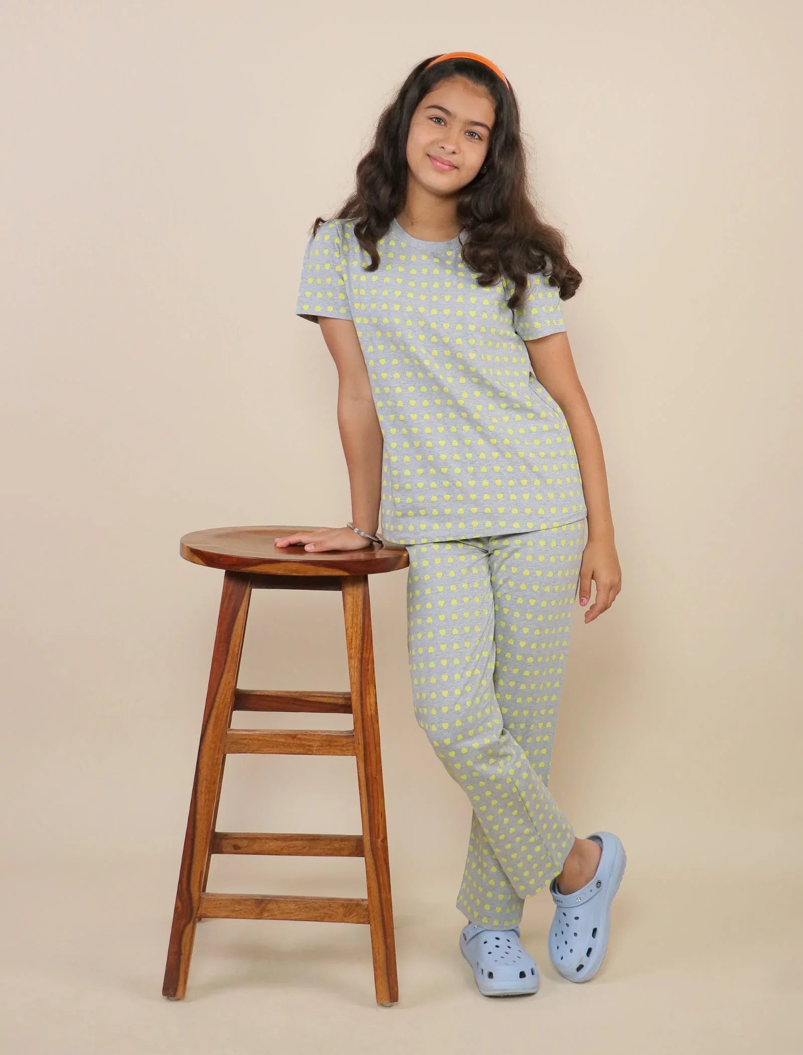 Girl wearing grey cotton night suit with yellow heart print, standing by wooden stool