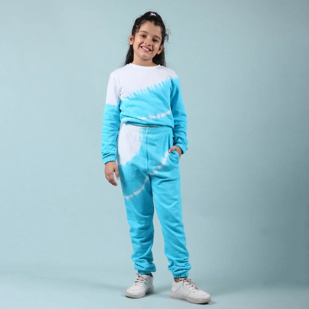 Smiling girl wearing blue and white tie-dye jogger set with sneakers, standing against light blue background