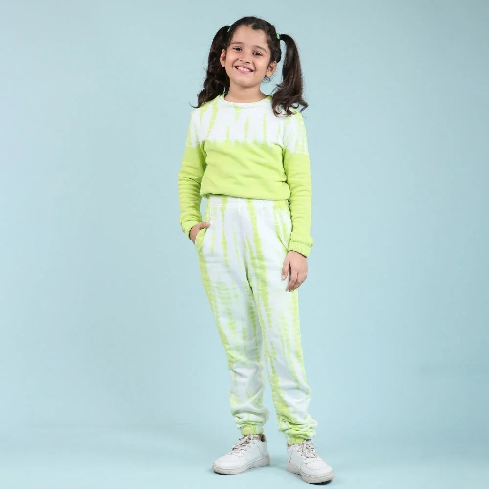 Smiling girl in light green and white tie-dye jogger set with white sneakers on blue background