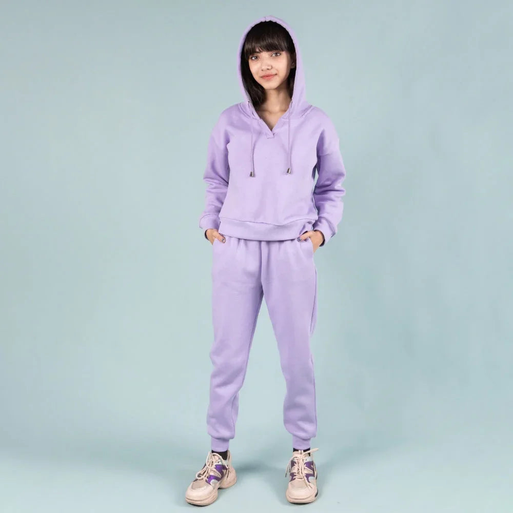 Girl wearing a lavender joggers set with hoodie and sneakers, standing against a plain background.