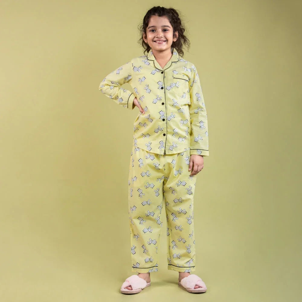Girl wearing yellow printed night suit set with pajama pants and slippers, standing and smiling