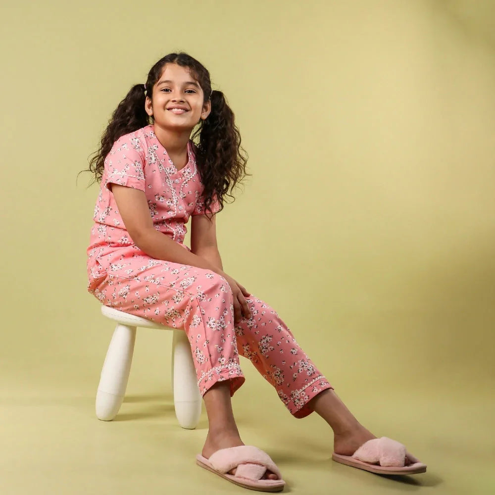 Girl wearing pink floral night suit and slippers sitting on stool against plain background