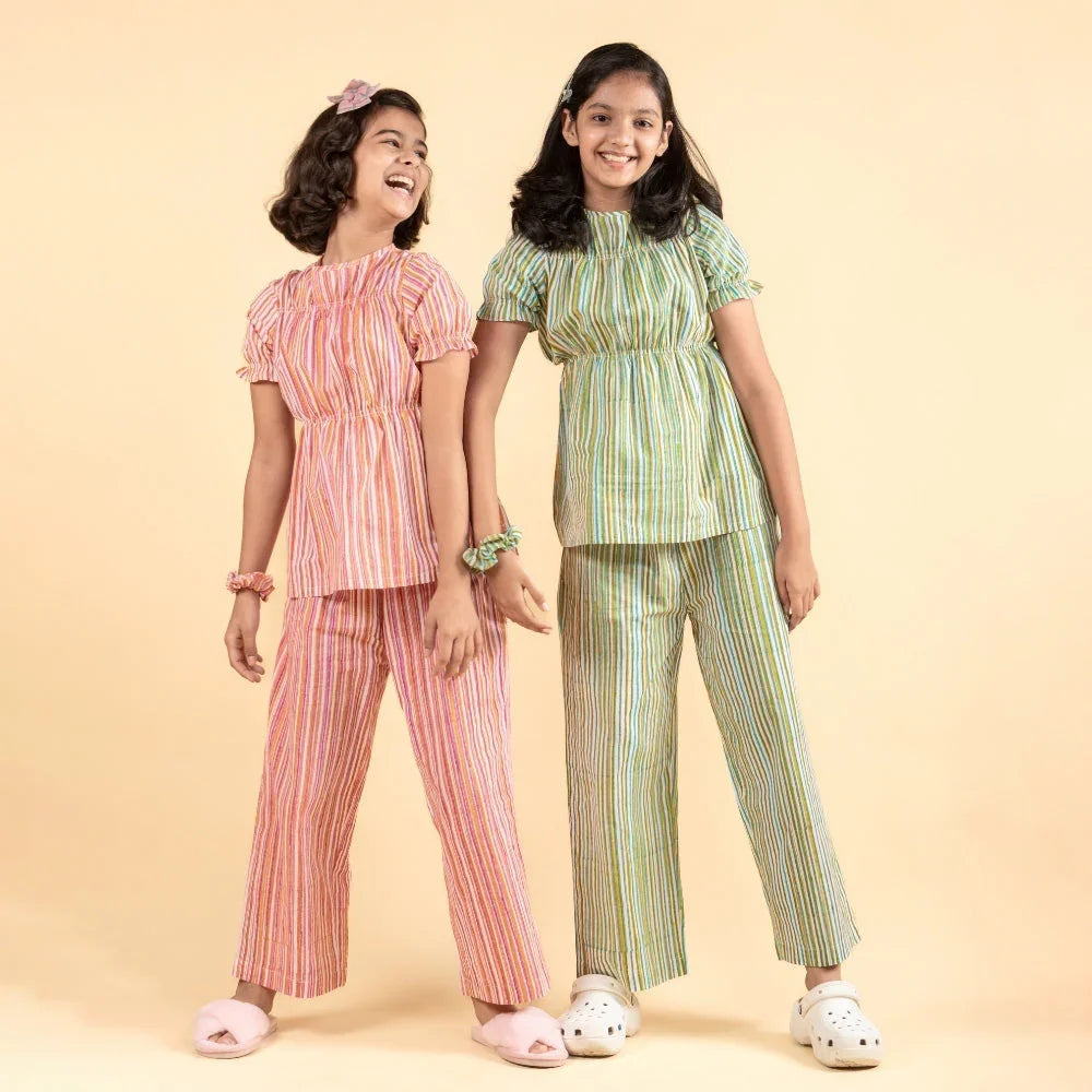 Two girls in striped cotton night suits with pants, smiling on a beige background