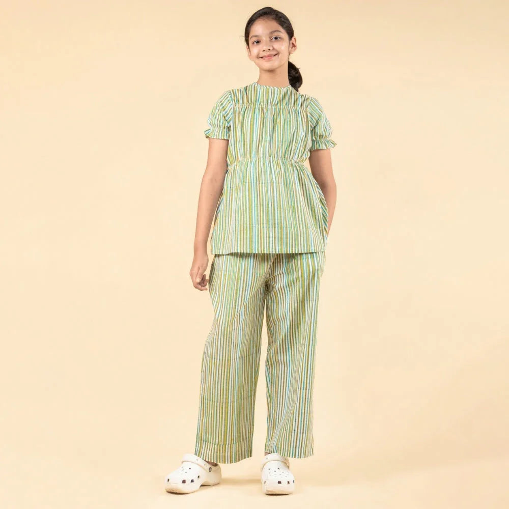 Teen girl wearing a striped green cotton night suit set, standing against a beige background