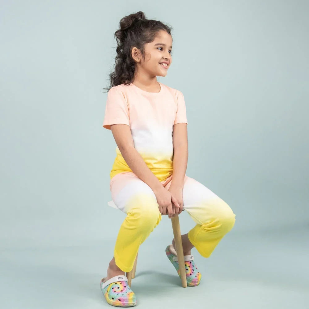 Smiling girl in pastel yellow and peach night suit for girls, sitting on a stool, studio background
