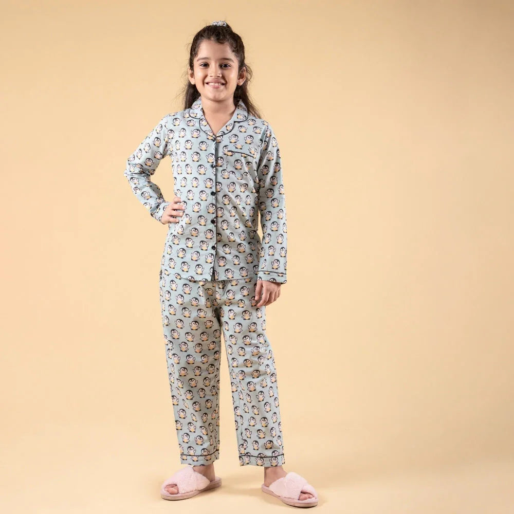 Girl wearing matching penguin print night suit and slippers, standing against beige background