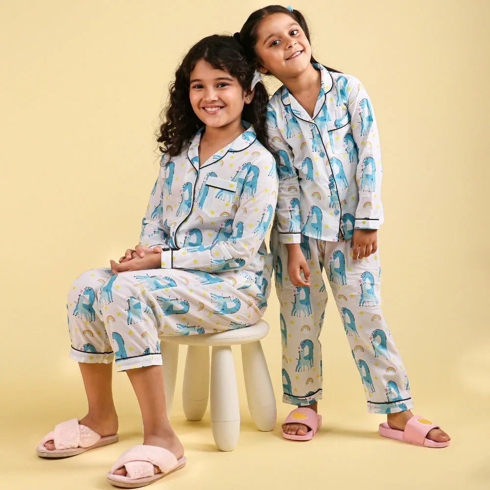 Two girls wearing matching dinosaur print night suits for girls, smiling in a studio setting.