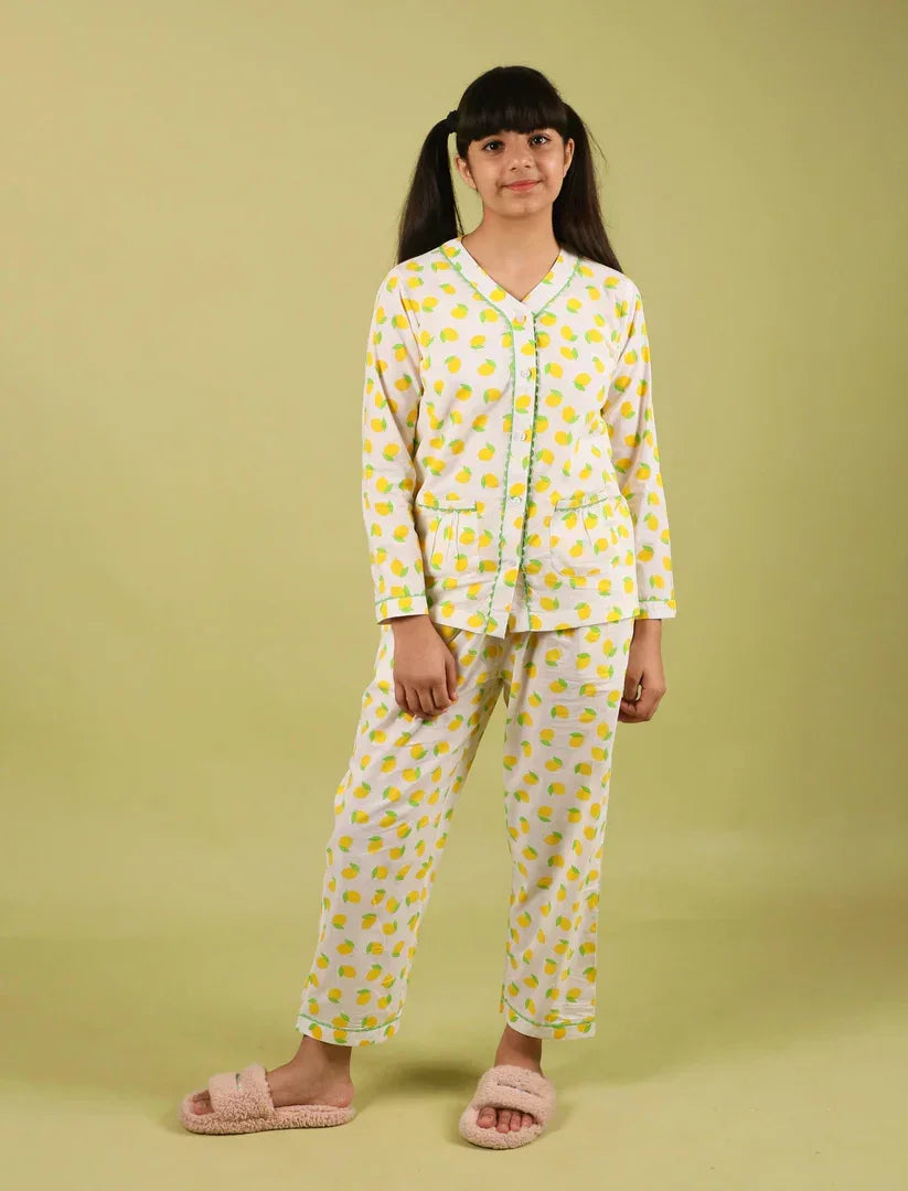 Girl wearing lemon print nightdress pajama set with pink slippers, standing indoors