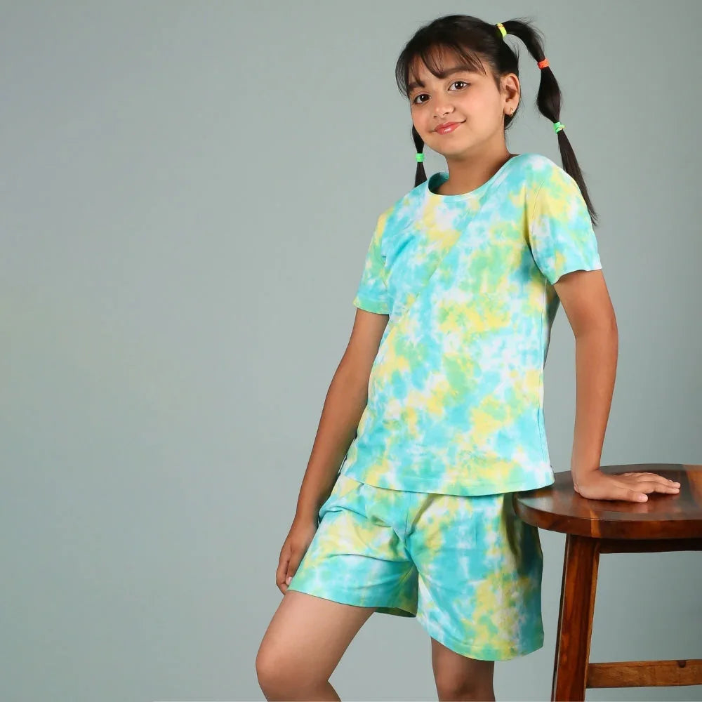 Preteen girl in blue and yellow tie-dye nightdress set, posing indoors by a stool