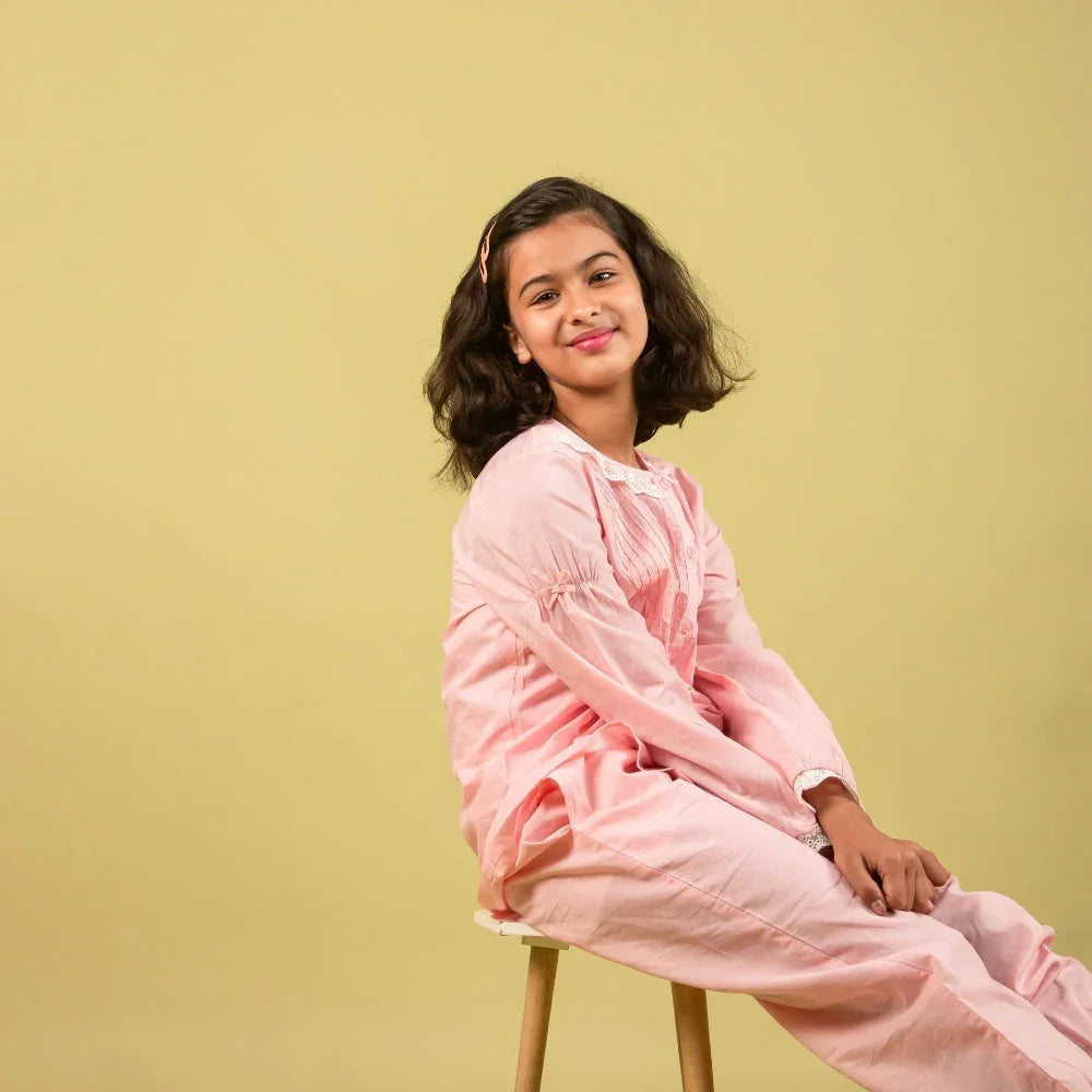 Smiling girl in pink nightdress for 6 years olds sitting on a stool against yellow background