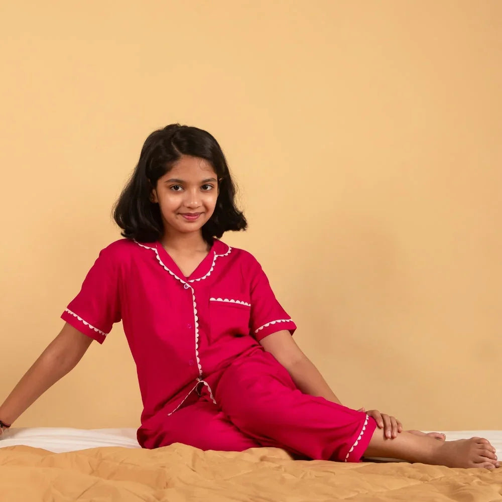 Smiling girl wearing red nightdress set with white trim, sitting on a bed