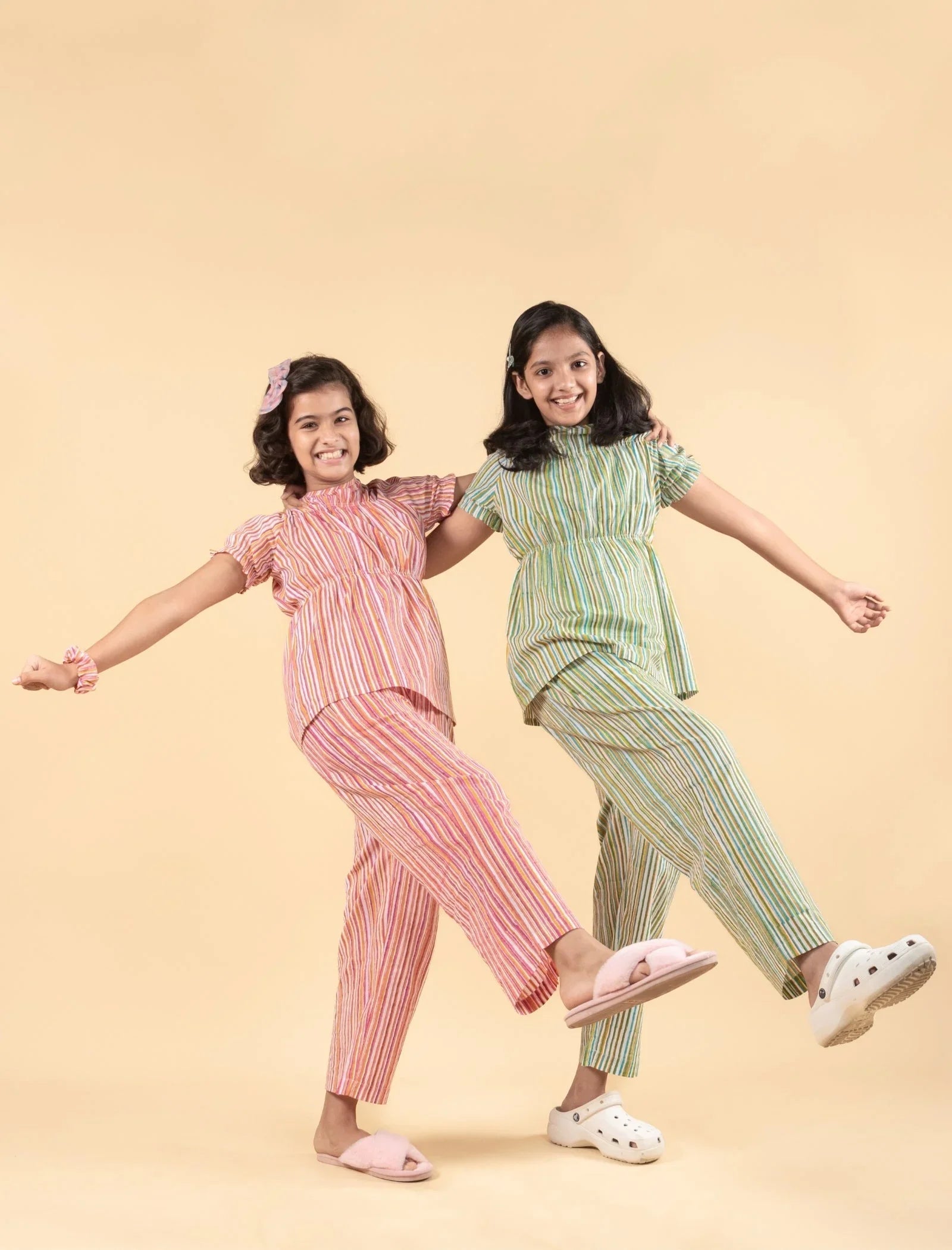 Two girls wearing striped nightdresses and pajamas posing playfully against a beige background