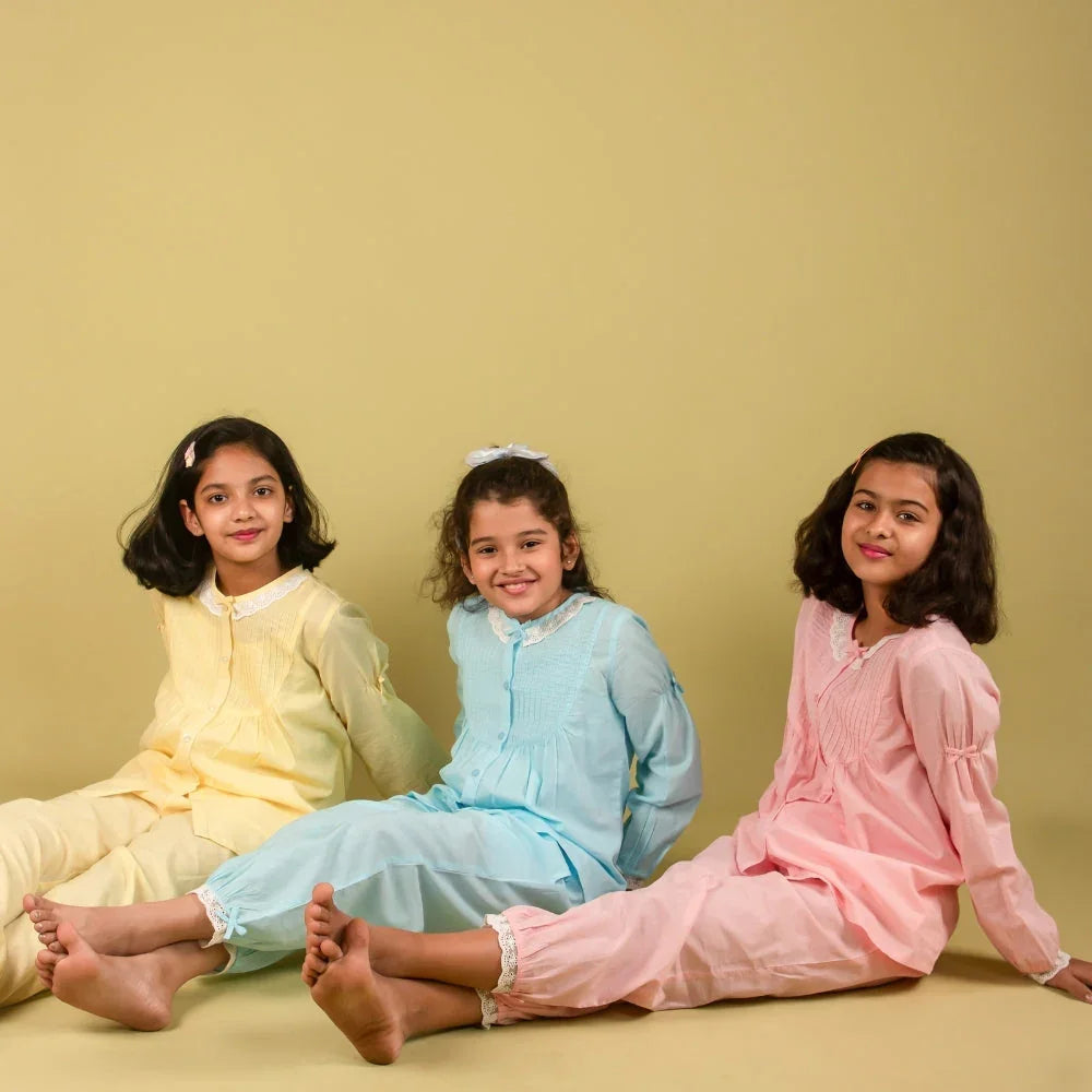 Three girls in pastel nightdresses sit on floor, kids sleepwear fashion, neutral background
