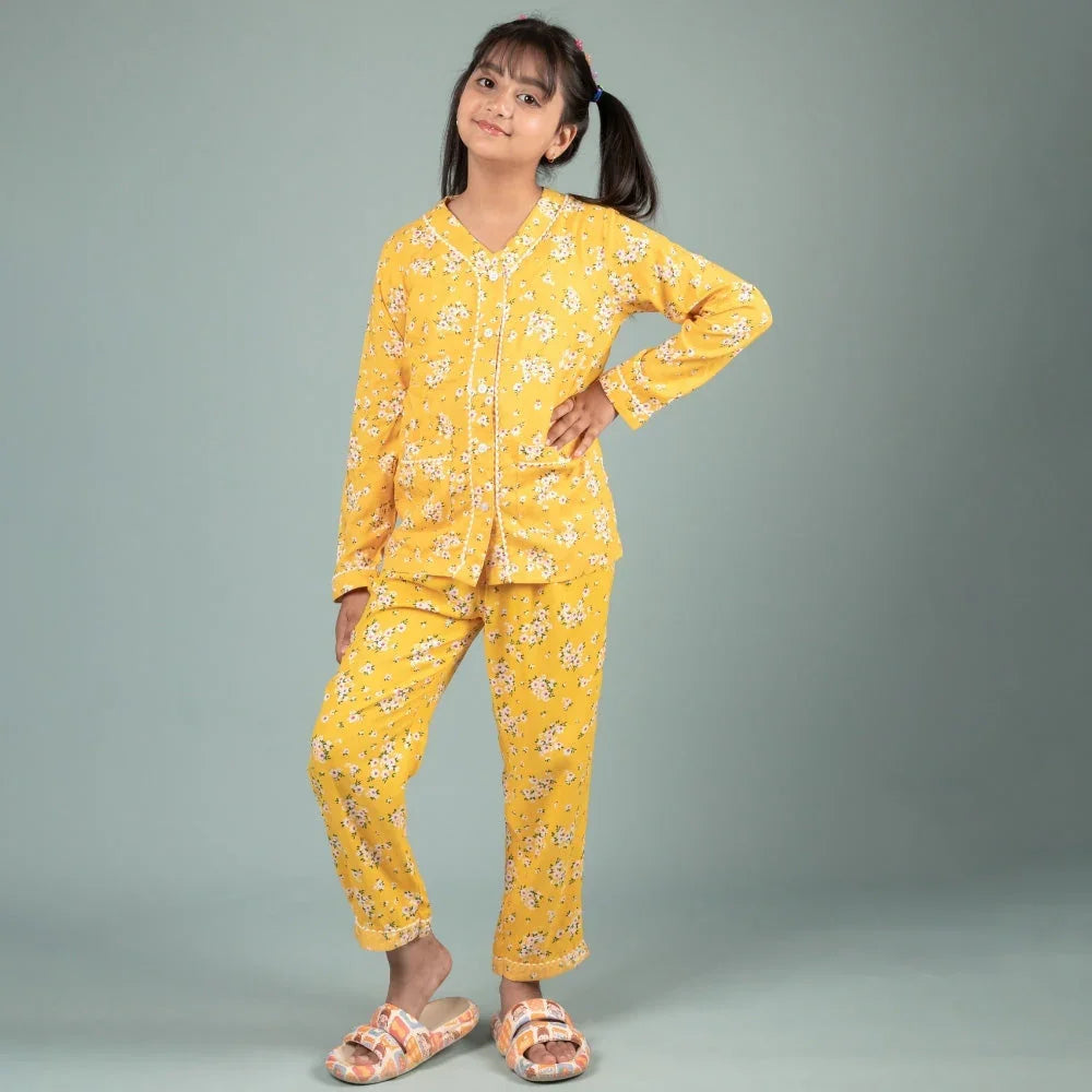 Girl wearing yellow floral night suit pajamas set for kids, standing against grey background