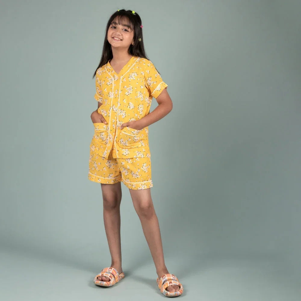 Girl wearing yellow floral nightwear shorts set, hands in pockets, standing on light background
