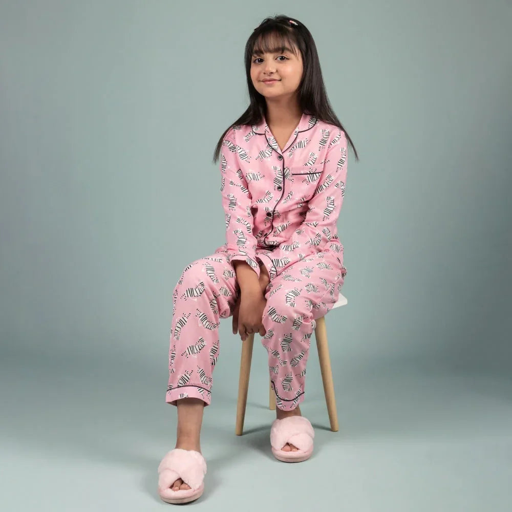 Girl in pink zebra print nightwear and slippers sitting on a stool against plain background