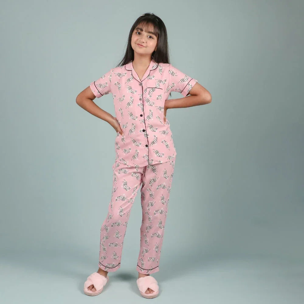 Teen girl in pink printed nightwear set and slippers posing on plain background