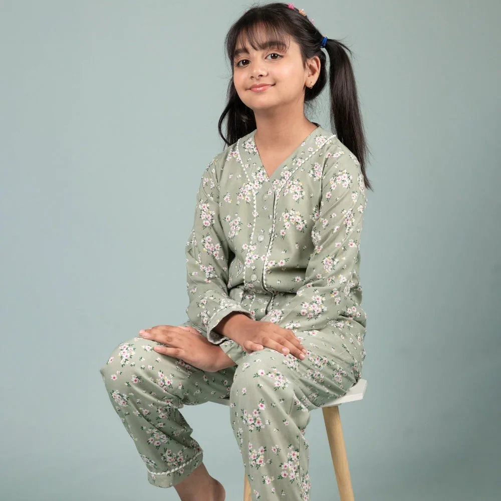 Girl in green floral print nightwear set, long sleeves, sitting on a stool, studio background