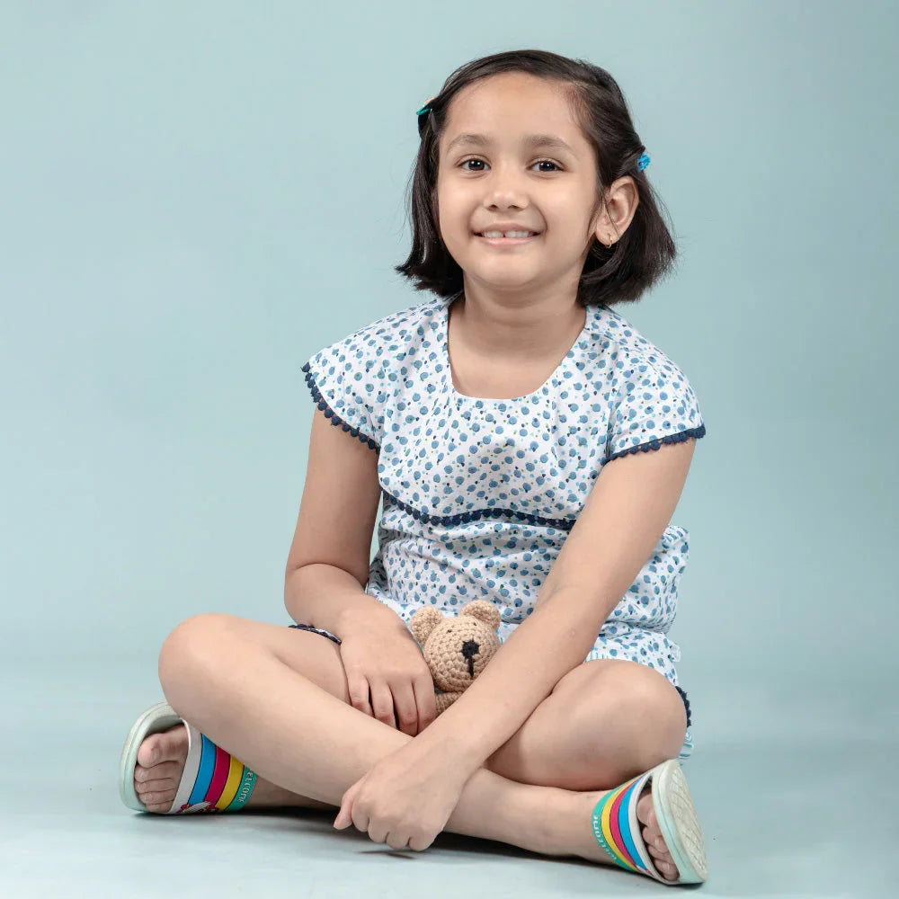 Smiling young girl in printed nightwear holding a small teddy bear, sitting cross-legged