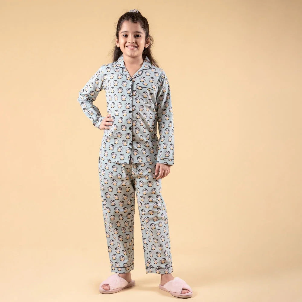Smiling girl in penguin print nightwear set and pink slippers against beige background