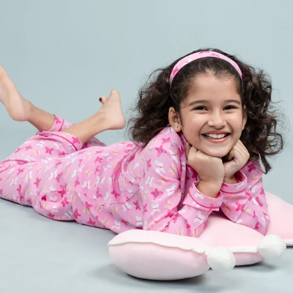 Smiling girl in pink butterfly print nightwear lying on a pillow, kids sleepwear fashion