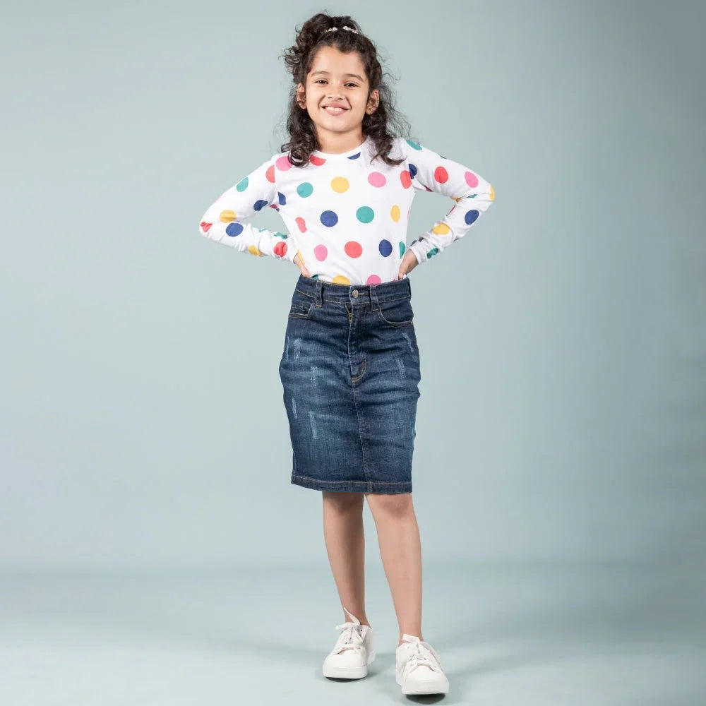 Smiling girl wearing a denim skirt, white polka dot top, and white sneakers