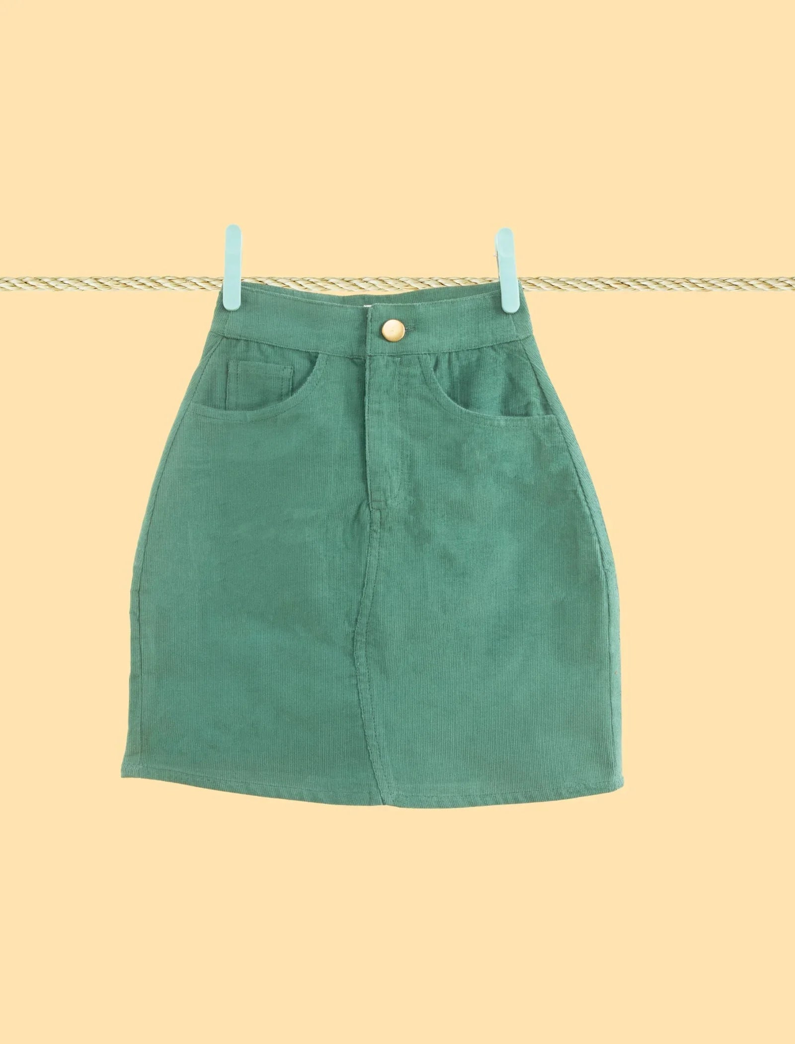Green corduroy skirt for girls, front view, with pockets, hanging on a clothesline