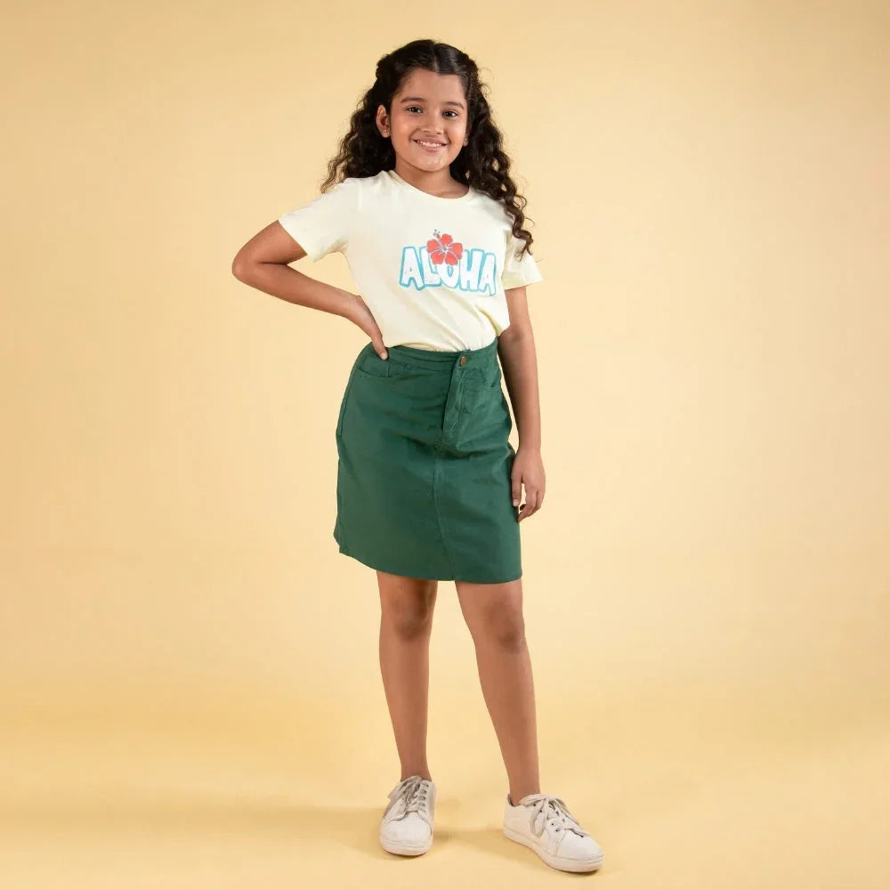 Smiling girl wearing green skirt and cream aloha t-shirt, posing on beige background