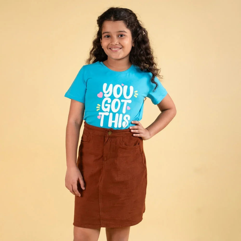 Smiling girl wearing a blue t-shirt with slogan and brown skirt, kids fashion outfit