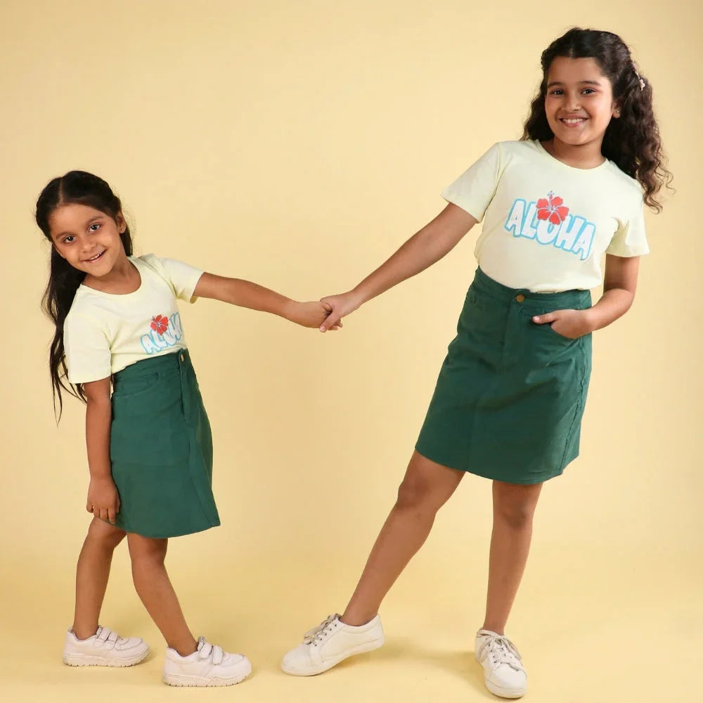 Two girls wearing green skirts and yellow aloha t-shirts, holding hands, smiling