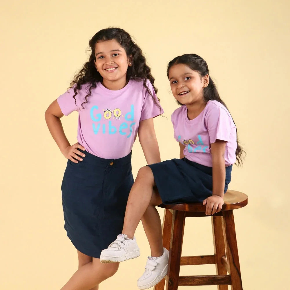 Two girls in matching lilac Good Vibes t-shirts and navy skirts, casual kidswear fashion