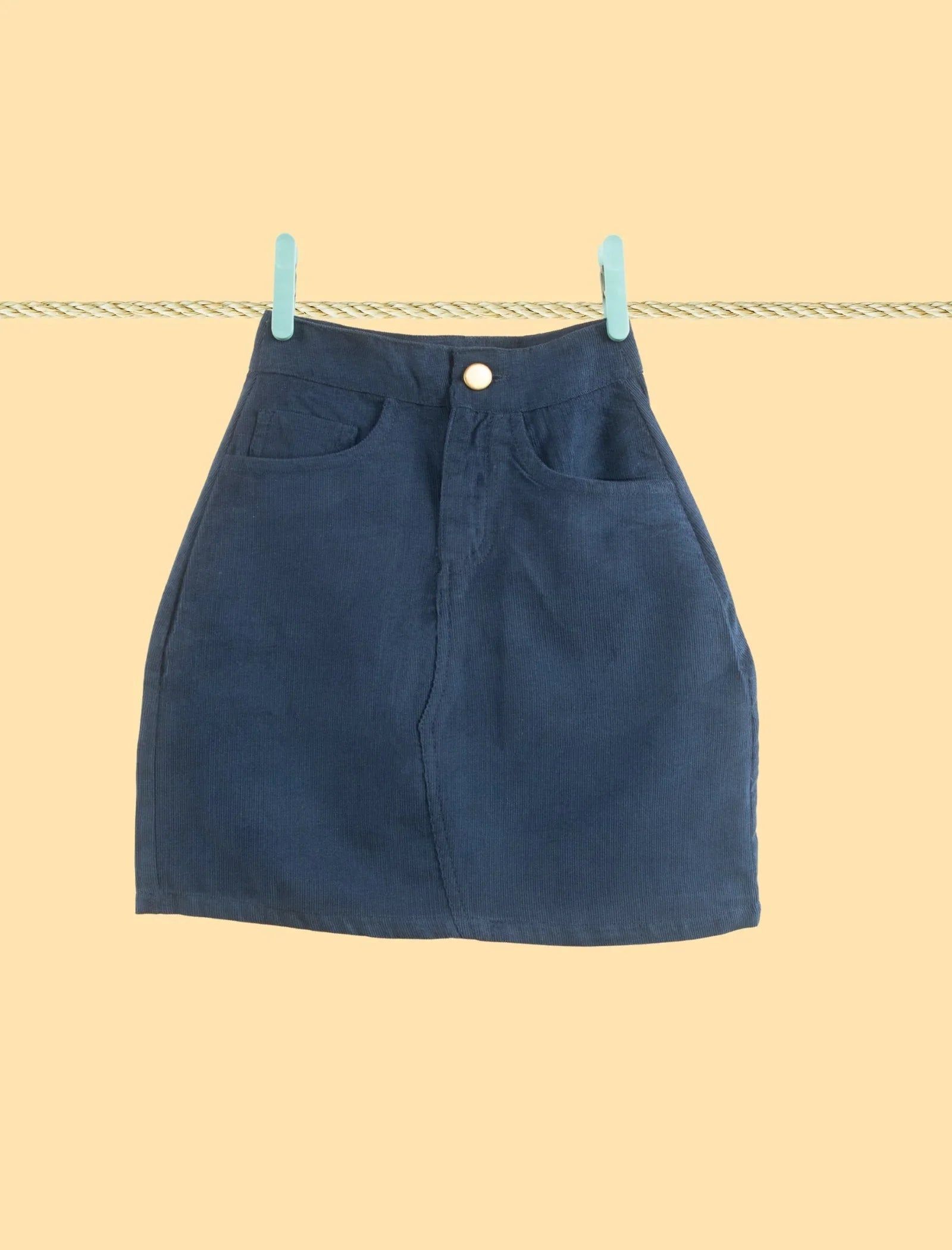 Dark blue corduroy skirt for girls with front pockets, displayed on a beige background