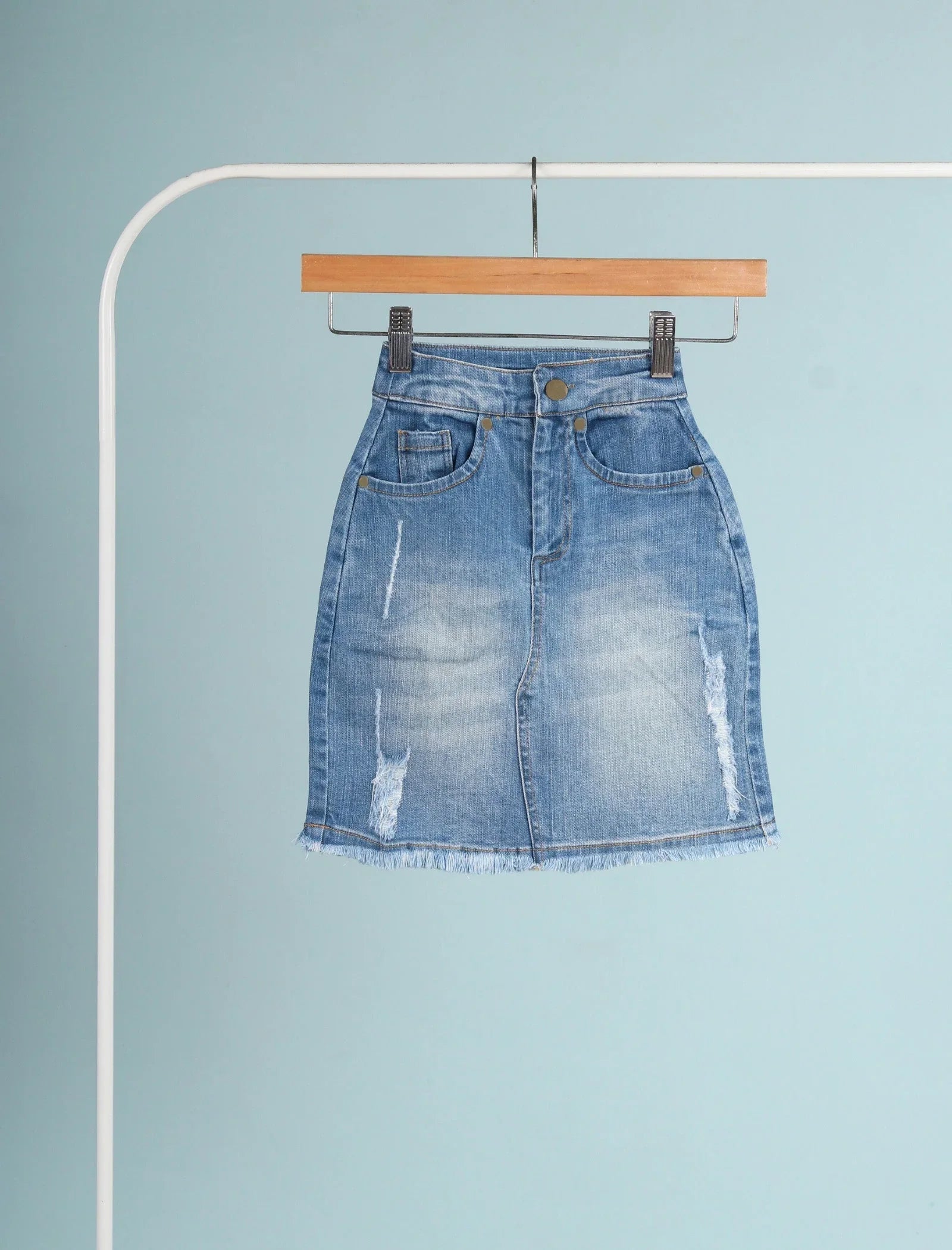 Girls’ blue denim skirt with front pockets, distressed details, and frayed hem on hanger
