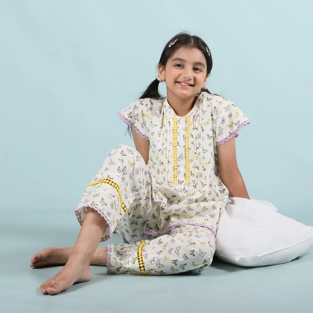 Smiling girl in butterfly print sleepwear set sitting on a pillow against light blue background