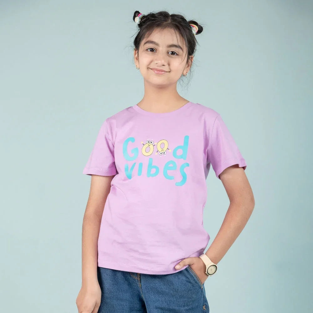 Smiling girl wearing a purple Good Vibes t-shirt and blue jeans, kids fashion outfit
